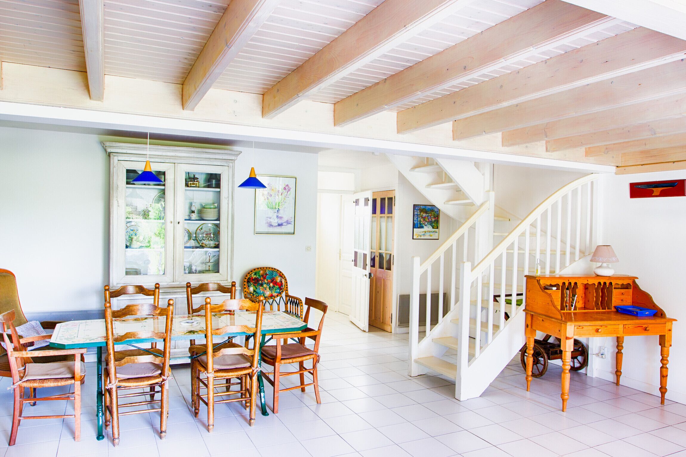 Un comedor con mesa y sillas de madera, un armario con puertas de vidrio y una escalera que sube a otro nivel.