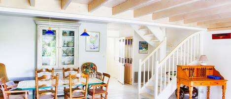 Un comedor con mesa y sillas de madera, un armario con puertas de vidrio y una escalera que sube a otro nivel.