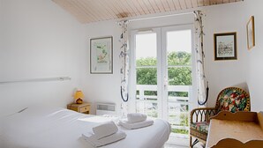A bedroom with a bed, a nightstand, a chair, and a window with curtains. - House for 6 in the heart of Saint Martin (Saint-Martin-de-Ré)