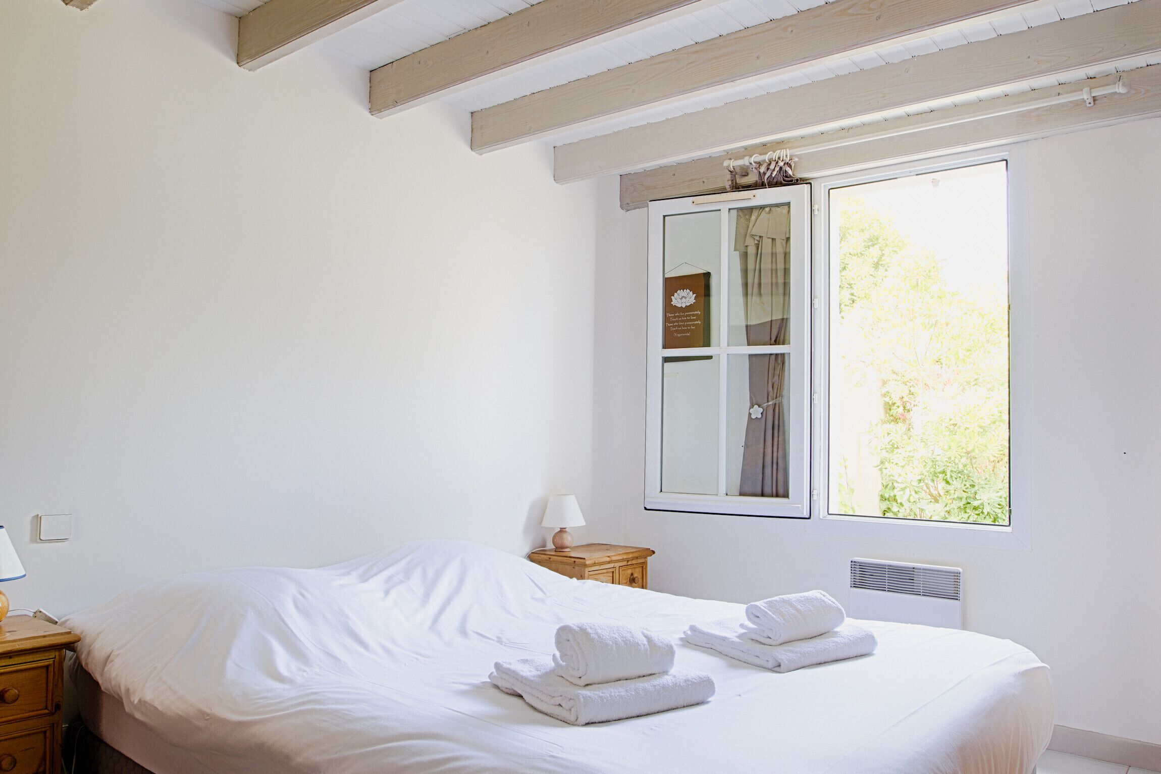 A bedroom with a bed, a nightstand, a lamp, and a window with a view of greenery.