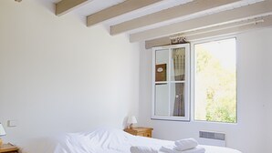 A bedroom with a bed, a nightstand, a lamp, and a window with a view of greenery. - House for 6 in the heart of Saint Martin (Saint-Martin-de-Ré)