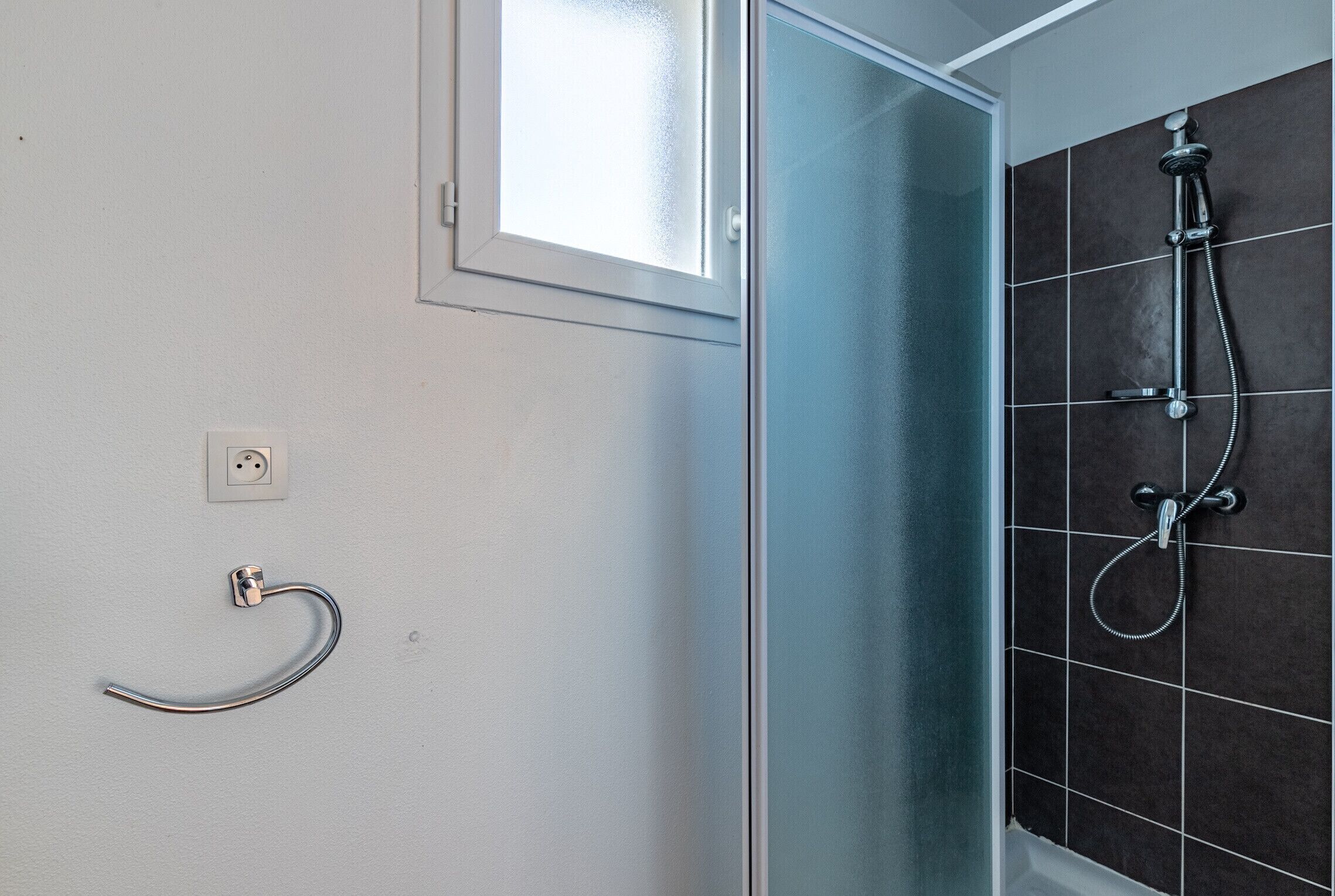 Une salle de bain avec une douche à parois de verre, un porte-serviettes et un interrupteur fixé au mur.