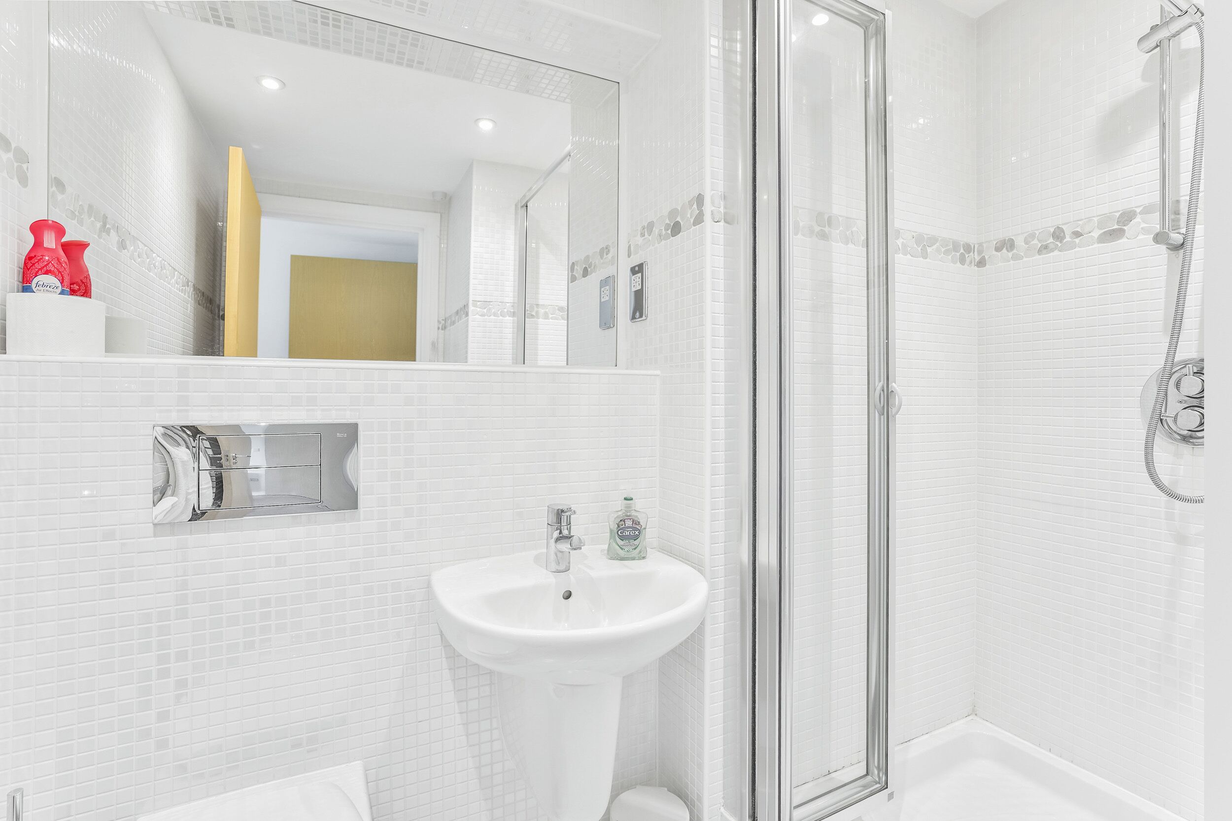 Ein modernes Badezimmer mit einem weißen Waschbecken, einer Duschkabine aus Glas und einem großen Spiegel.
