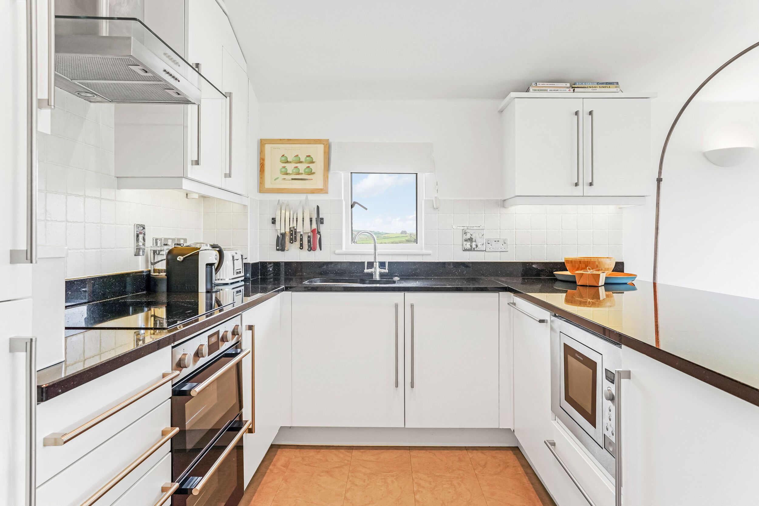 A modern kitchen with white cabinetry, a black countertop, and stainless steel appliances.