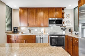 A modern kitchen with wooden cabinets, stainless steel appliances, granite countertops, and a built-in oven.