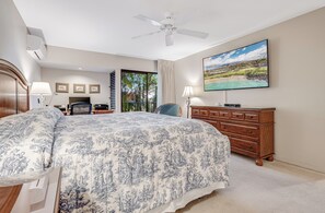 A bedroom with a large bed, a ceiling fan, a TV, a dresser, and a view of the outdoors. - Beautiful Ground Floor Oasis: Workspace & Serene Surroundings -Wailea Elua 2501 (Wailea, Maui)