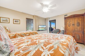 Een slaapkamer met twee bedden, een plafondventilator, een televisie en een garderobe.