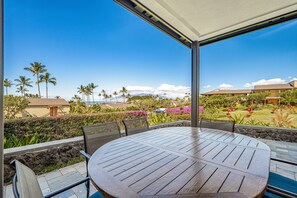 Une terrasse extérieure avec une table ronde et des chaises, donnant sur un jardin aménagé avec des palmiers et offrant une vue sur l’océan.