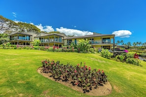A hotel with multiple two-story buildings, a well-maintained lawn, and a variety of tropical plants.