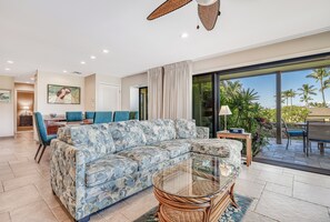 A modern living room with a sectional sofa, a glass coffee table, and a dining area with blue chairs.
