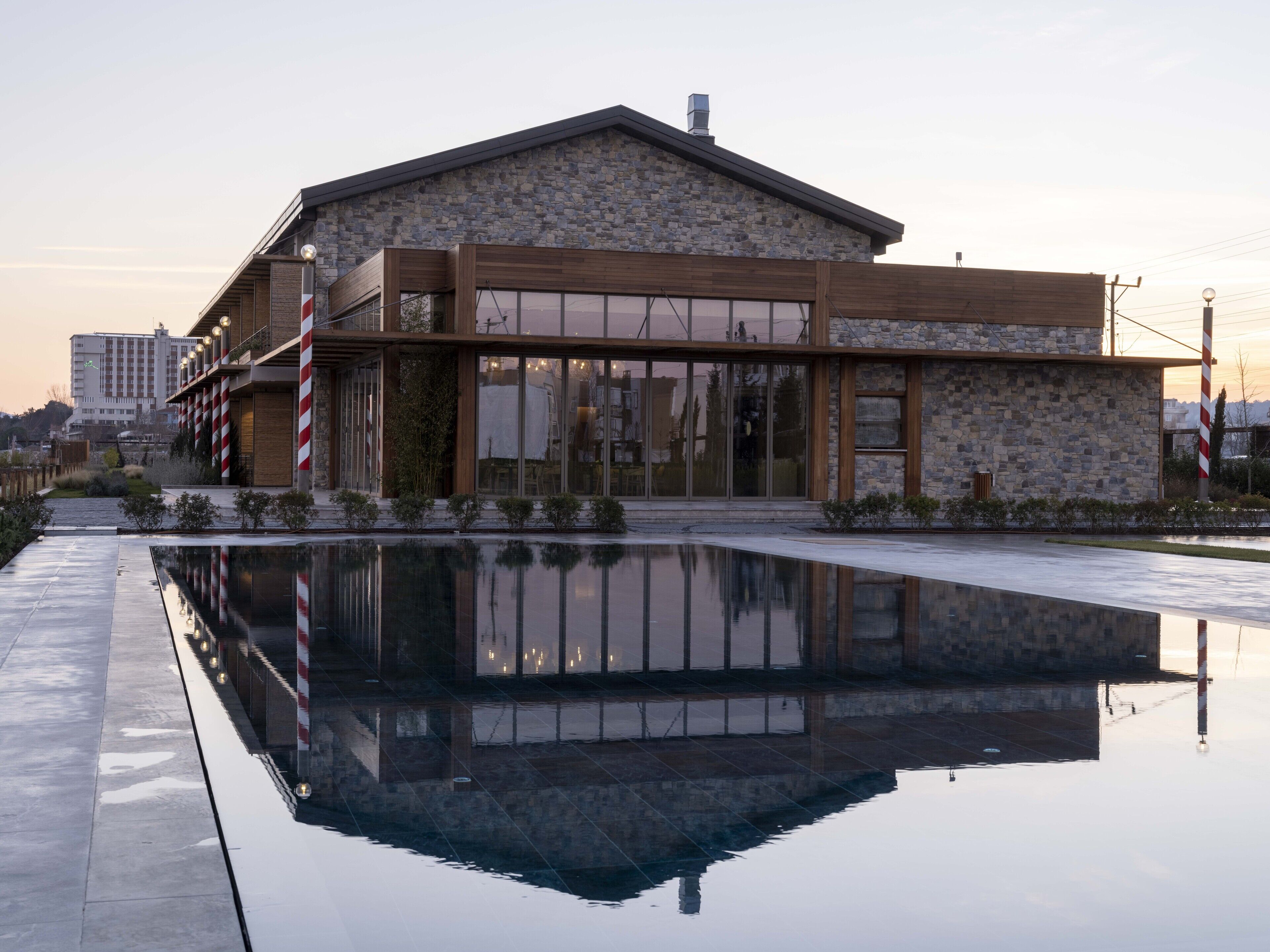Un edificio moderno con fachada de piedra, amplios ventanales y reflejo en el agua.