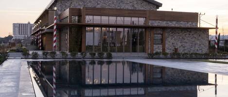 Un edificio moderno con fachada de piedra, amplios ventanales y reflejo en el agua.