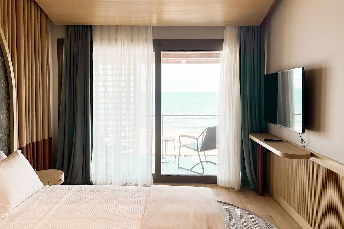 A hotel room with a bed, a TV, a balcony with a chair, and curtains.