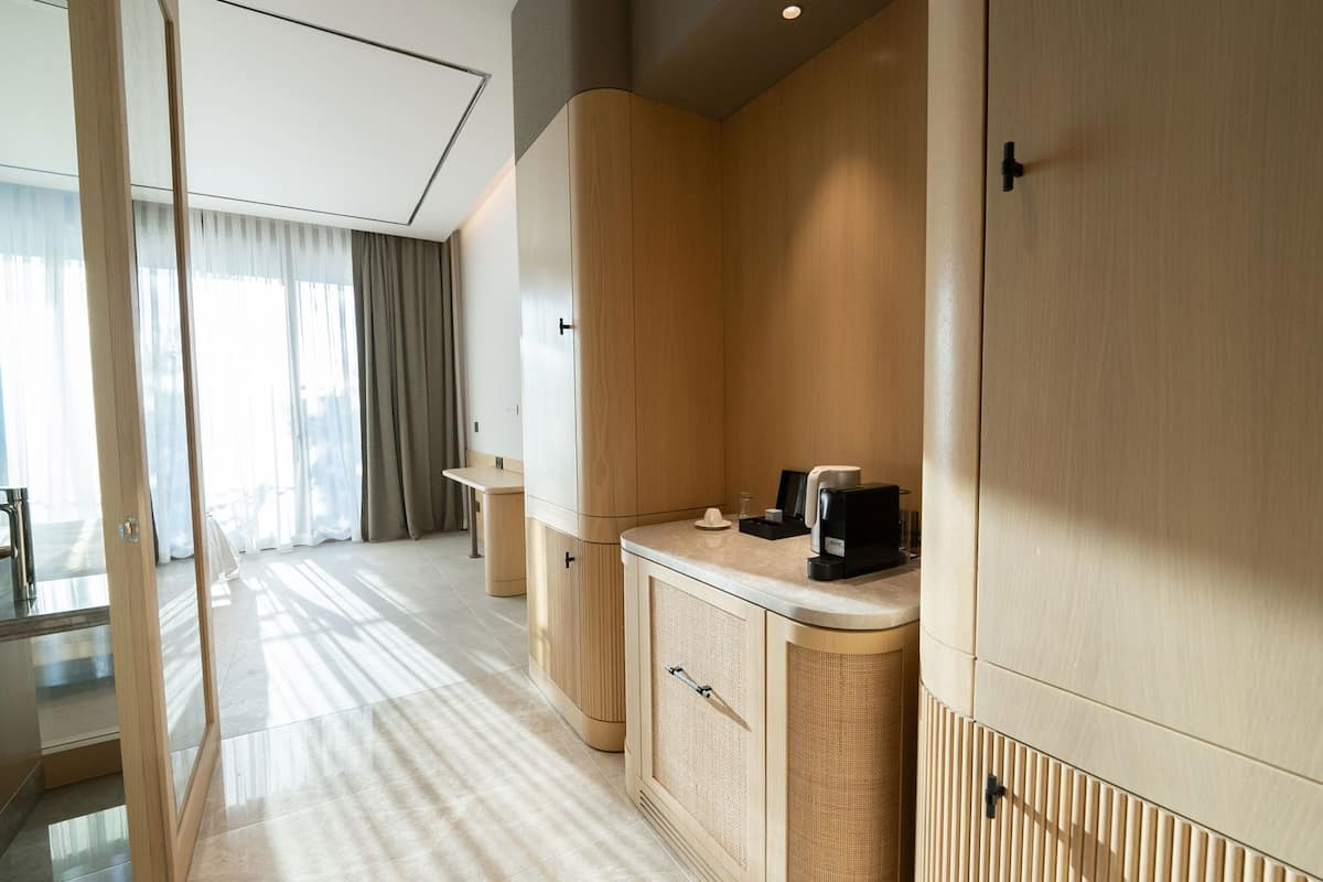 A modern hotel room with a kitchenette, a seating area, and a large window with curtains.