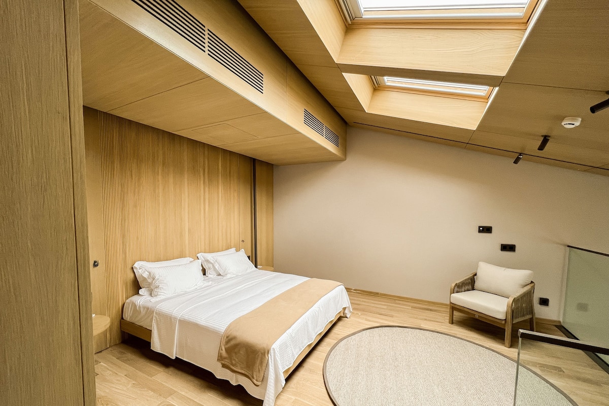 A modern bedroom with a skylight, a bed, a chair, and a round rug.
