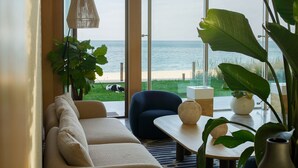 A modern living room with a sofa, a coffee table, and a view of the sea through large windows.