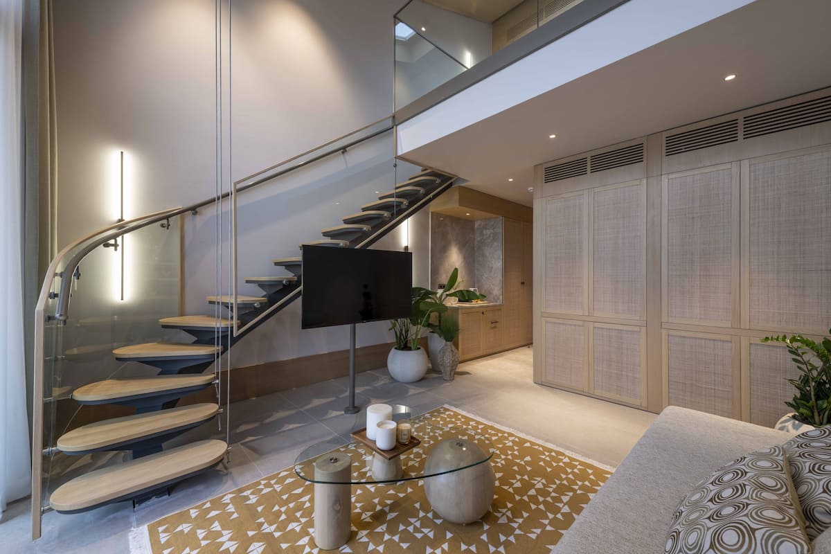 A modern interior with a glass staircase, a flat-screen TV, and a patterned rug.