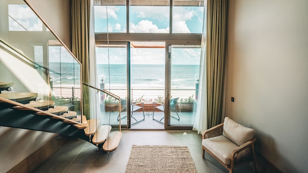 A modern interior with a staircase leading to a balcony overlooking the sea.