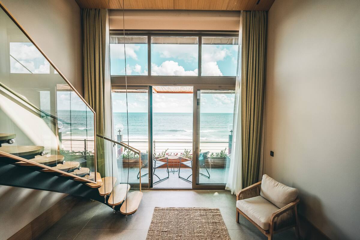 A modern interior with a staircase leading to a balcony overlooking the sea.