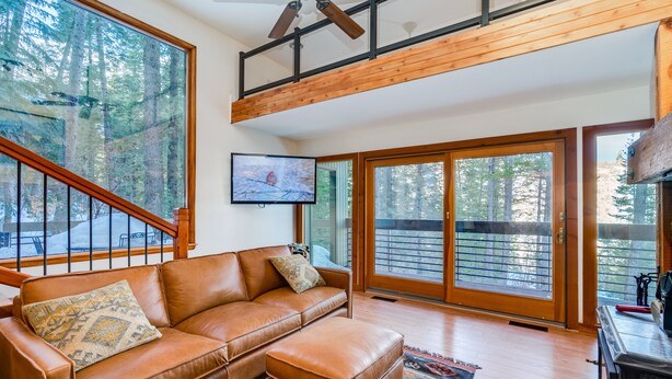 Ein geräumiges Wohnzimmer mit einer Ledersofa, einem Fernseher und großen Fenstern mit Blick auf den Wald.