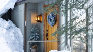 Eine Holztür mit einem Kranz, einer kleinen Weihnachtstanne und einer Laterne an der Wand.