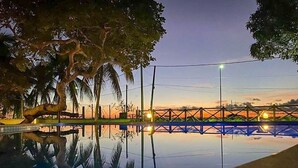 A tranquil outdoor pool area with a bridge and trees at dusk. - MSP02 Village 3 Quartos Pé na Areia (Cairu)
