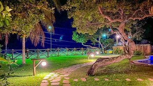 A nighttime garden with a stone pathway, a tree, and a fence. - MSP02 Village 3 Quartos Pé na Areia (Cairu)