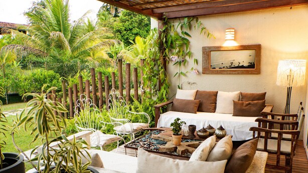 A cozy outdoor seating area with a sofa, chairs, and a table, surrounded by lush greenery and a wooden deck. - MSP02 Village 3 Quartos Pé na Areia (Cairu)