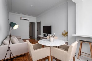 En moderne stue med sofa, rundt bord, gulvlampe, fjernsyn og en barstol.