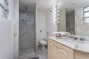 A bathroom with a shower, toilet, vanity, and mirror with lights.
