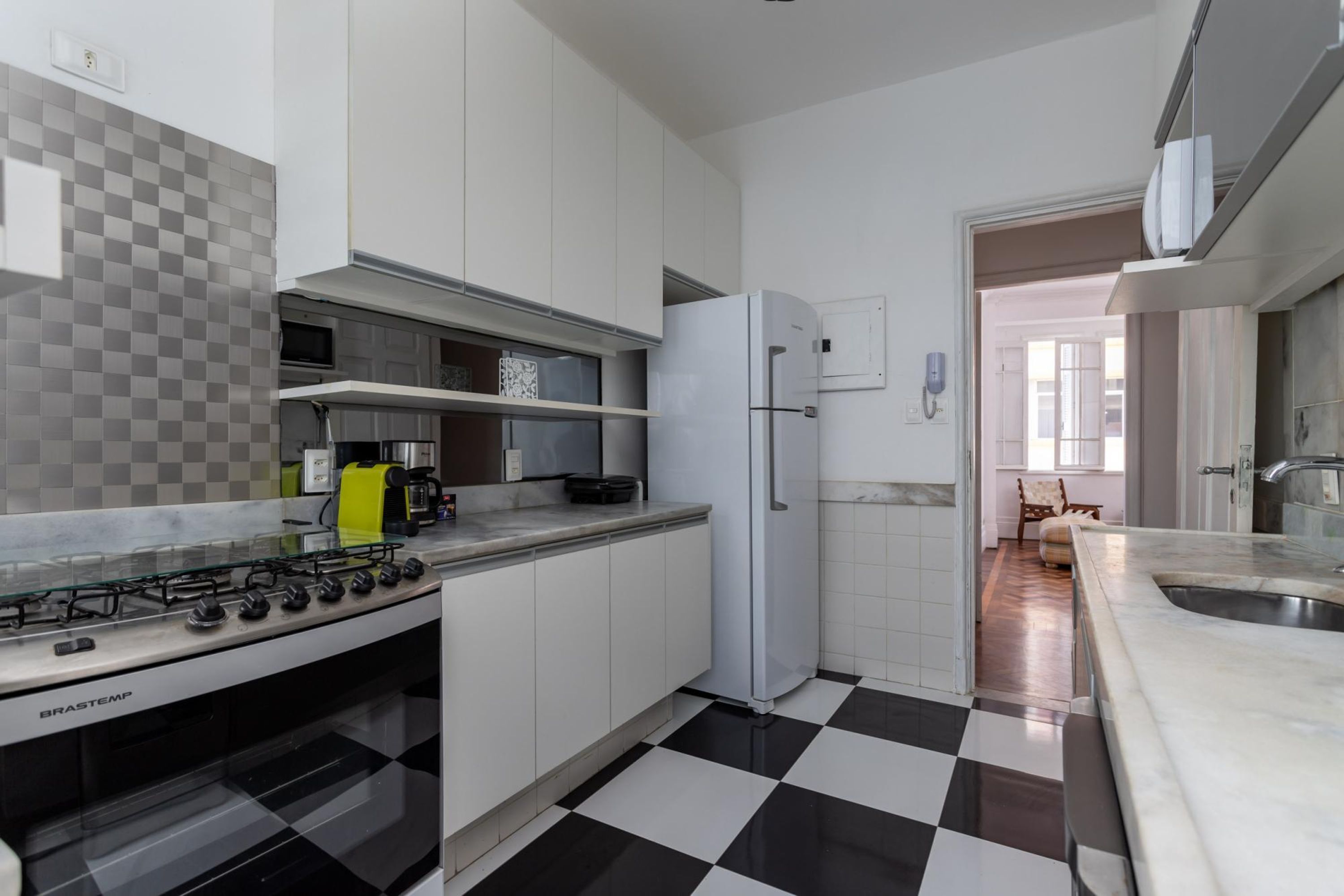 A kitchen with white cabinets, a gas stove, a refrigerator, and a checkered floor.