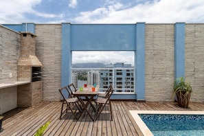 Una terraza en la azotea con zona de barbacoa, piscina y vistas de la ciudad.