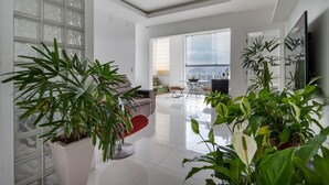 A modern living room with a glass dining table, a sofa, and several potted plants. - Coverage in Barra da Tijuca for 6 People Lc2207 (Rio de Janeiro)