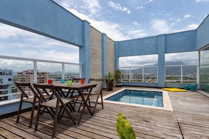 Terraza en la azotea con piscina, cubierta de madera y mesa con sillas.