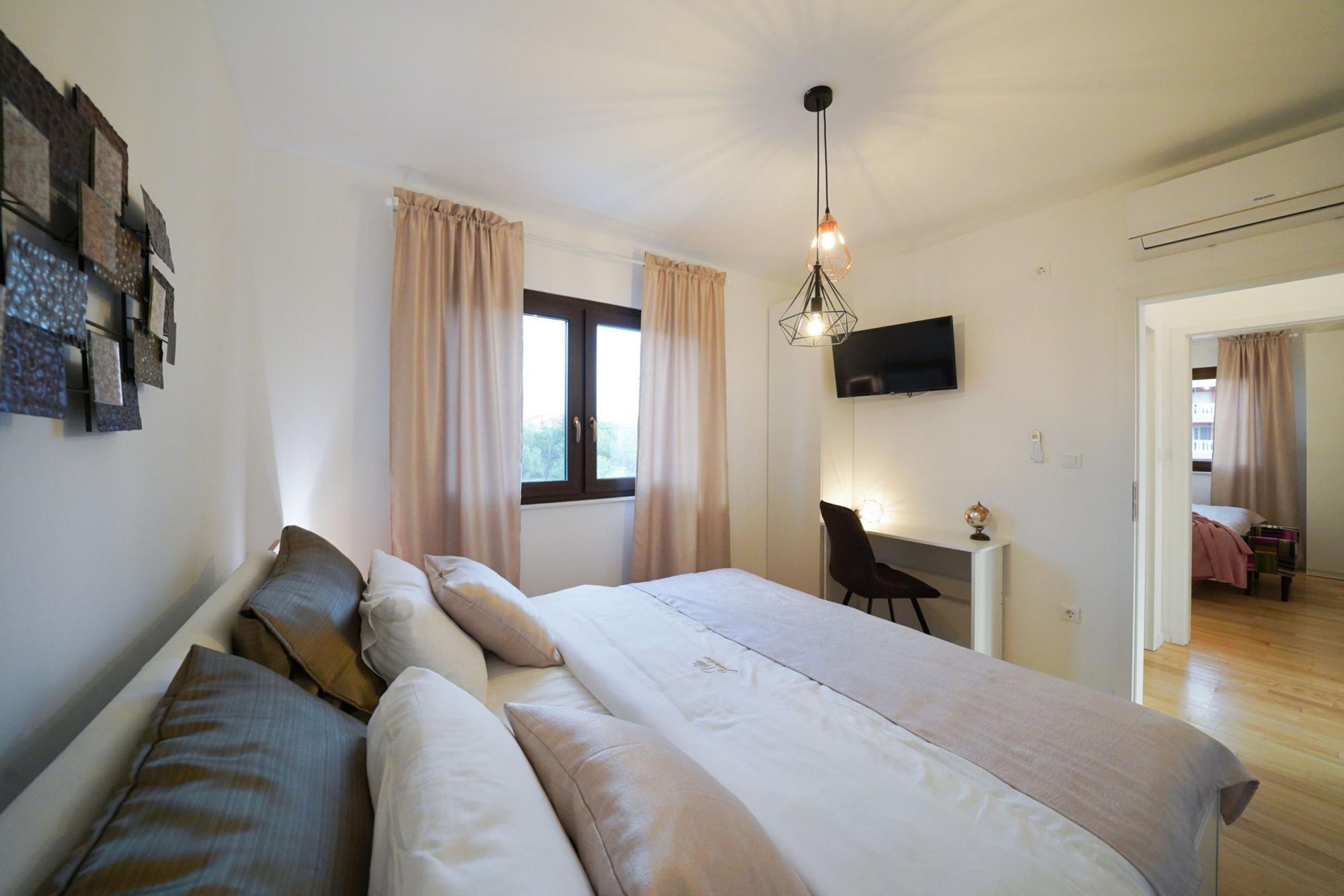 A bedroom with a large bed, a desk, a chair, a TV, and a window with curtains.