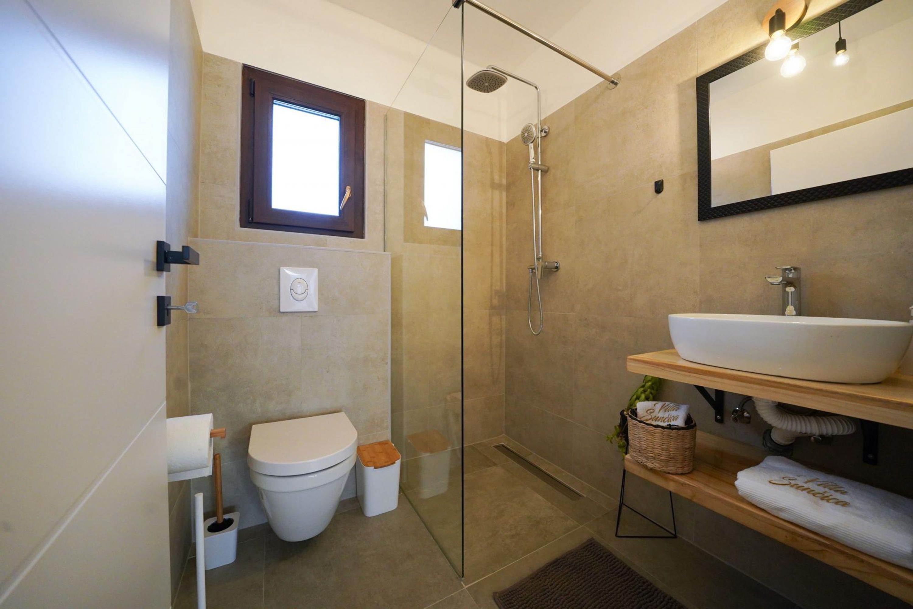 Un baño moderno con cabina de ducha de vidrio, inodoro blanco y tocador de madera con un lavamanos grande.