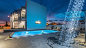 Een modern gebouw met een zwembad, terras en een fontein.