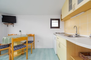 A compact kitchen with a dining table, chairs, a small window, and a television mounted on the wall. - Villa Petra Zadarvillas (Bibinje)
