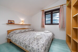 Ein Schlafzimmer mit einem Bett, einem Fenster mit Vorhängen, einem Regal mit einem Bild und einer Lampe sowie einem Holzschrank.