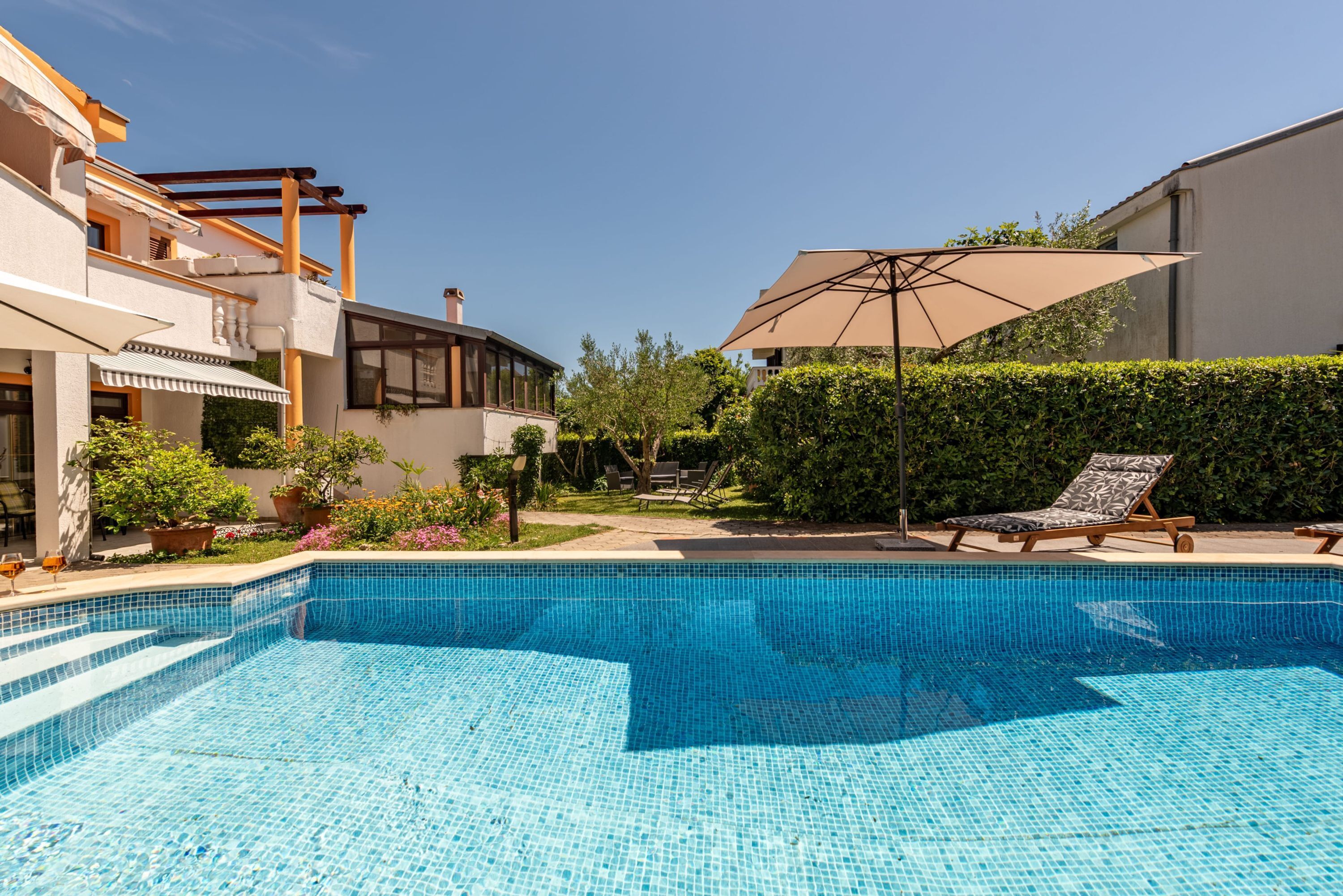 A swimming pool with tiled steps, surrounded by lounge chairs and a large umbrella.