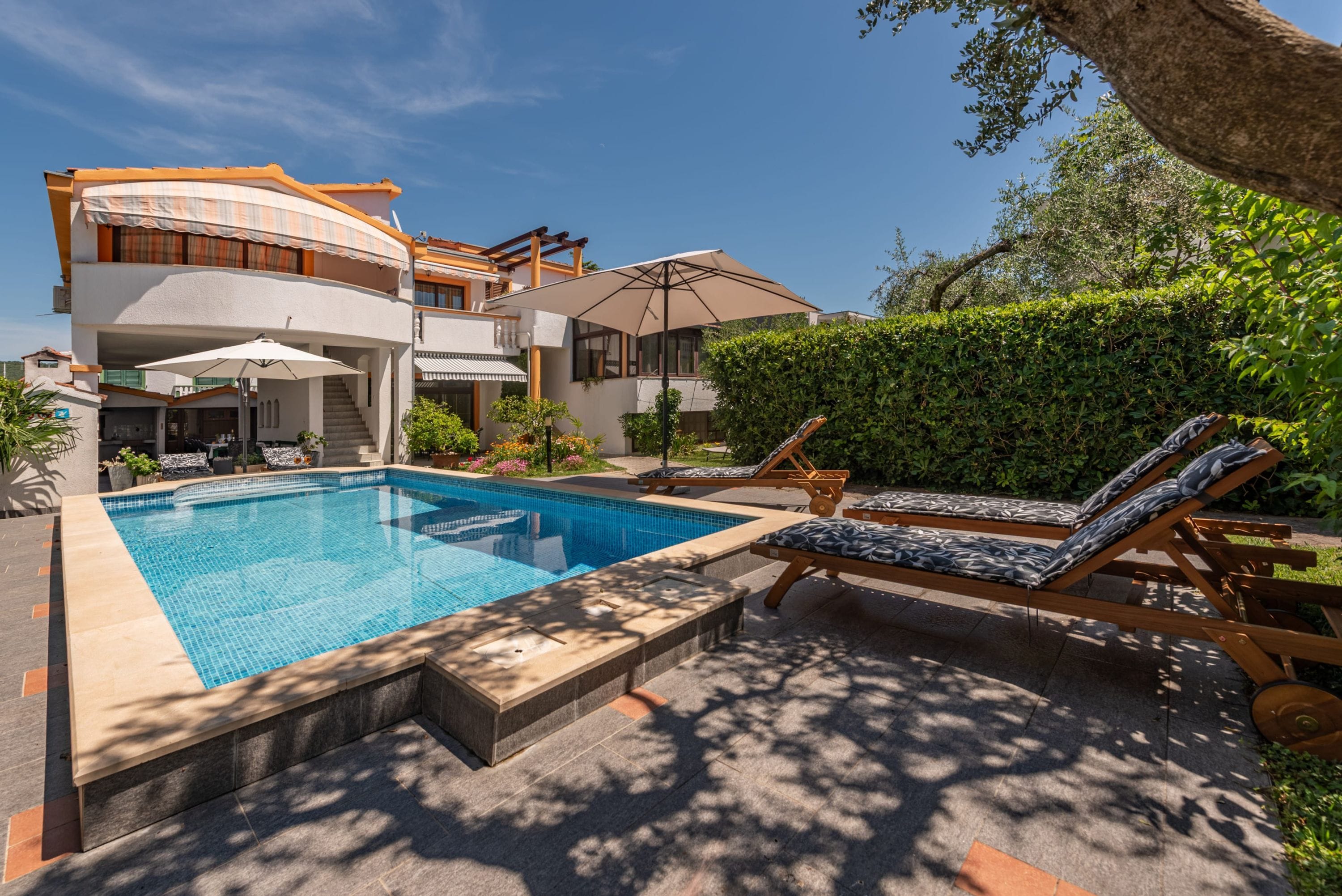 A modern two-story house with a swimming pool, lounge chairs, and a pergola.
