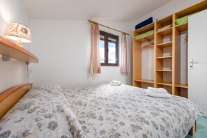 A bedroom with a bed, a window with curtains, a bedside lamp, a wardrobe, and a shelf with a lamp. - Villa Petra Zadarvillas (Bibinje)