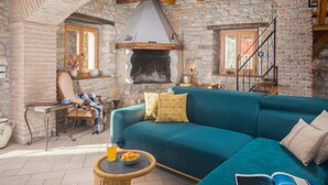 A cozy living room with a stone fireplace, a teal sofa, and a wicker table with snacks.