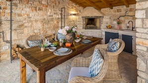 A rustic stone wall interior with a wooden dining table set for four, surrounded by wicker chairs.
