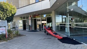 Entrada de hotel con fachada de vidrio, un kayak y un letrero de una pizzería.