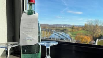 Eine Flasche Mineralwasser mit Etikett auf einer Fensterbank, mit Blick auf eine Brücke und die Landschaft.