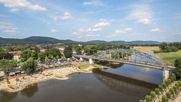 A river with a bridge, a beach with umbrellas, and a town in the background.