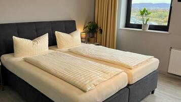 A double bed with a dark headboard, two pillows, and a bedside table with a lamp and a plant.