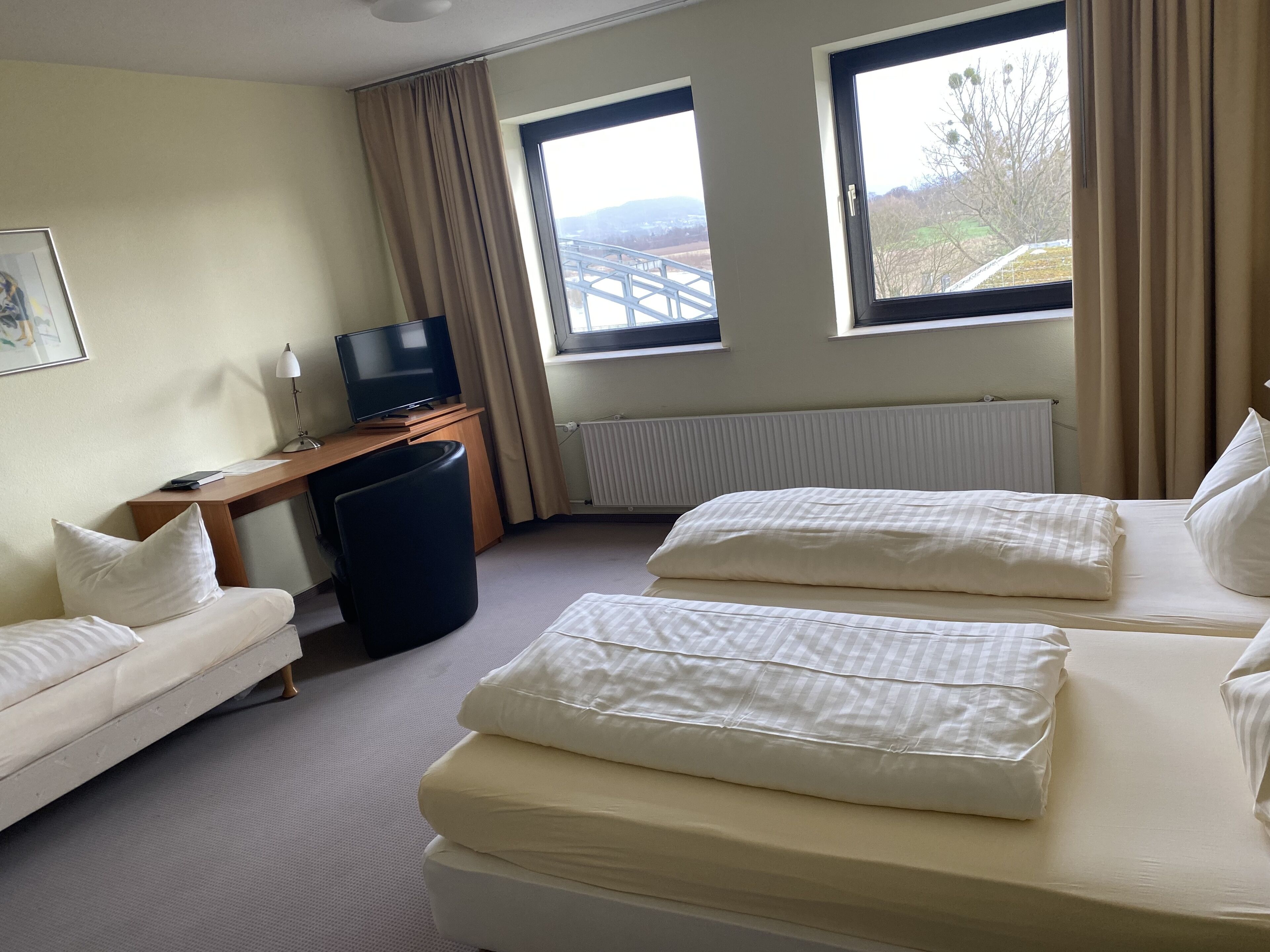 Hotellihuone, jossa on kaksi sänkyä, työpöytä, jossa on televisio, tuoli ja ikkuna, josta on näkymä sillalle.