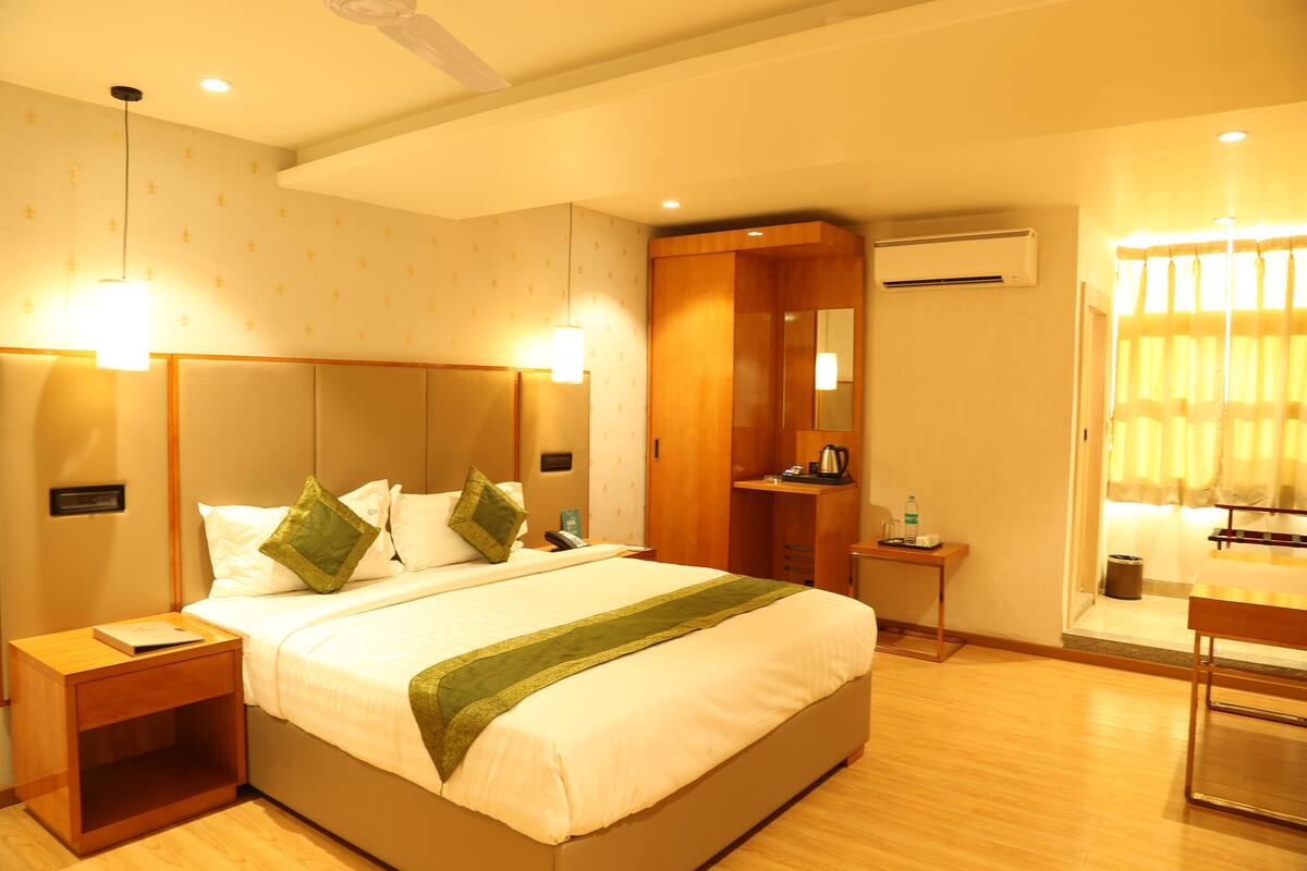Quarto de hotel com uma cama grande, mesas de cabeceira, guarda-roupa, espelho e ar condicionado.